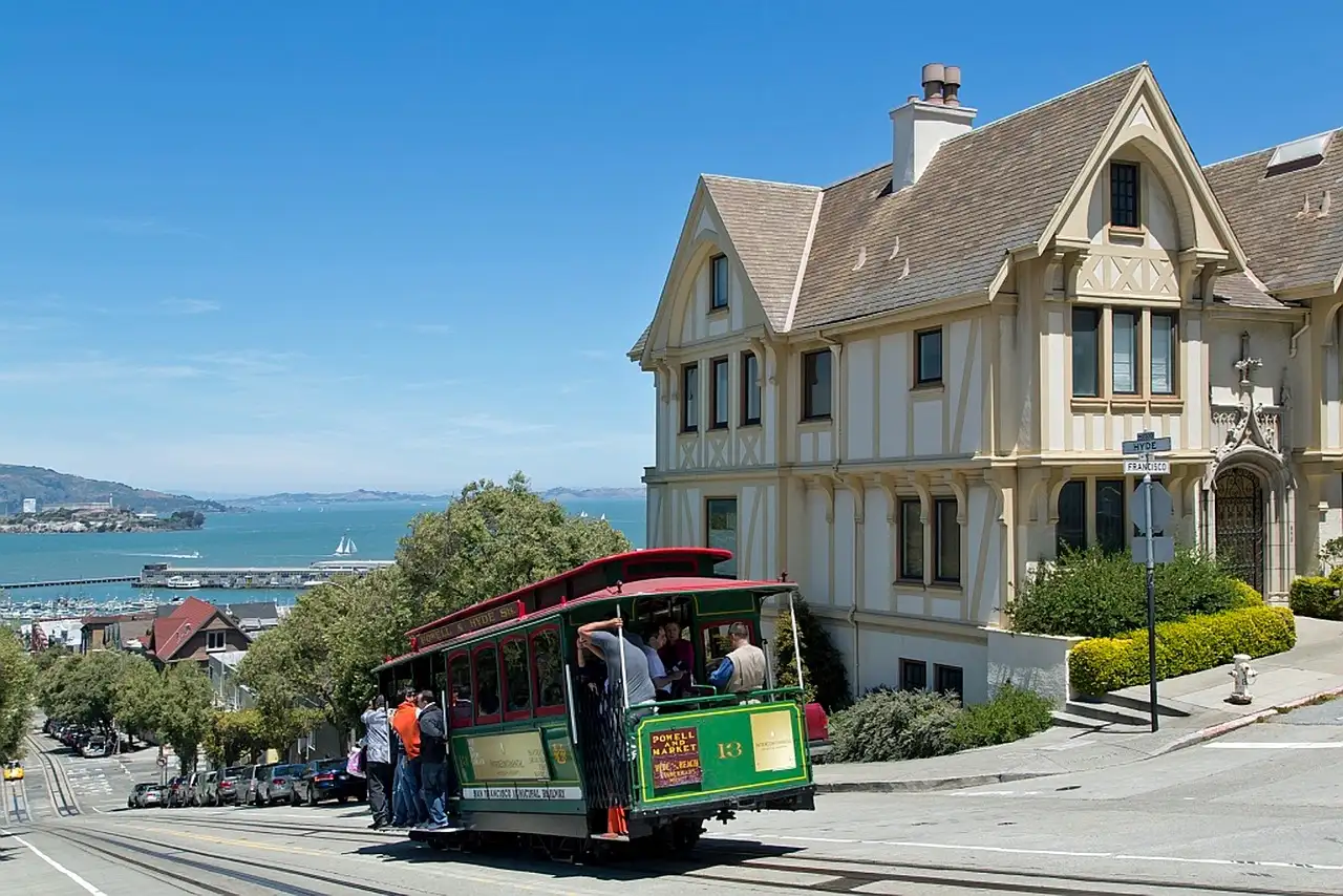 A cable car at the top of a hill with the bay and Alcatraz behind