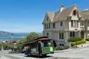A cable car at the top of a hill with the bay and Alcatraz behind