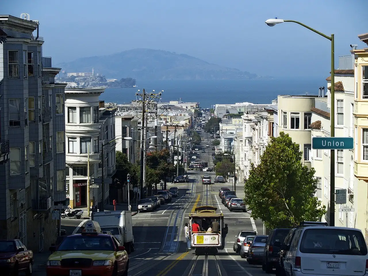 A cable car climbing Hyde Street with Alcatraz in the bay behind