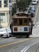A cable car on a steep street between parked cars