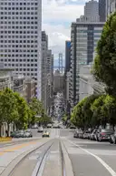 California Street running downhill between office towers, cable car tracks in front and the Bay Bridge at the end