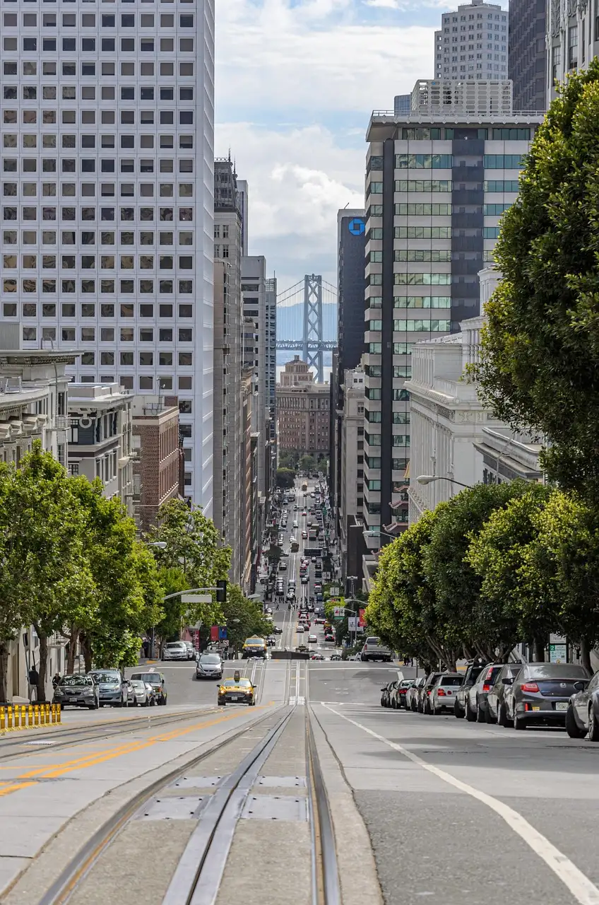 California Street running downhill between office towers, cable car tracks in front and the Bay Bridge at the end