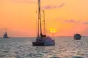 A catamaran on calm water at sunset, with other boats nearby