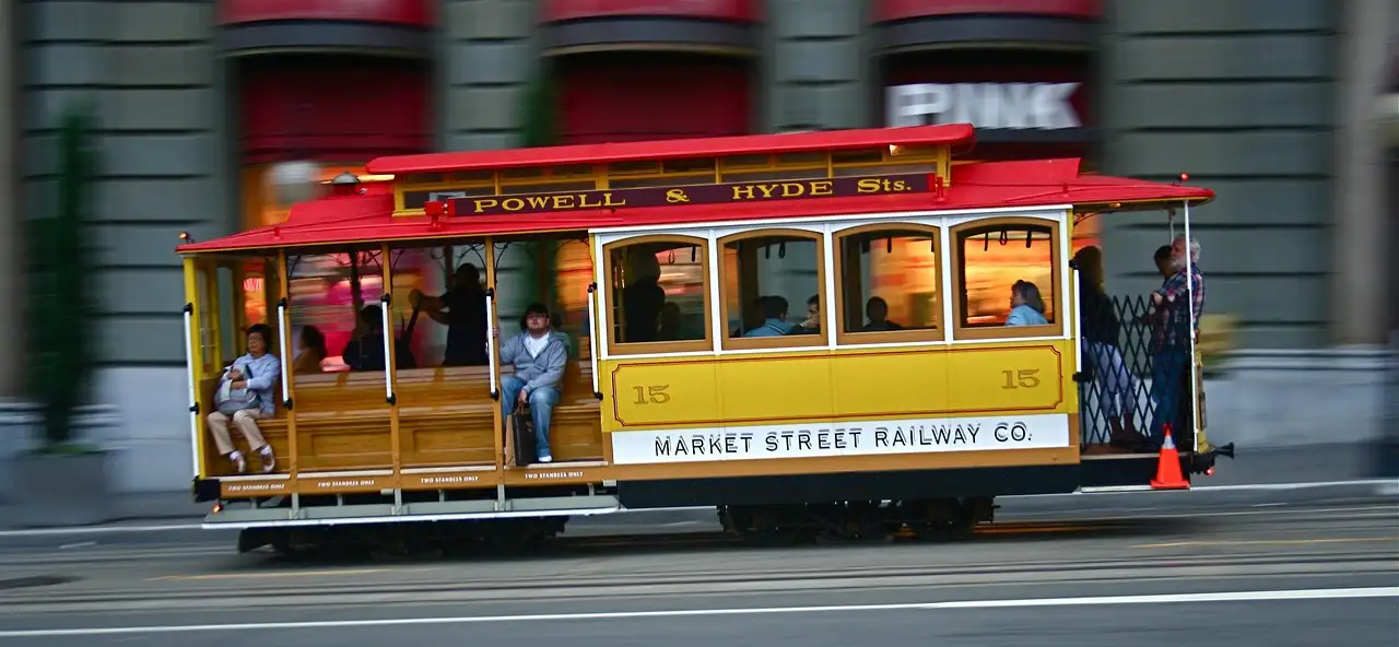 A yellow and red San Francisco cable car moving along Market Street in daylight