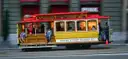 A yellow and red San Francisco cable car moving along Market Street in daylight