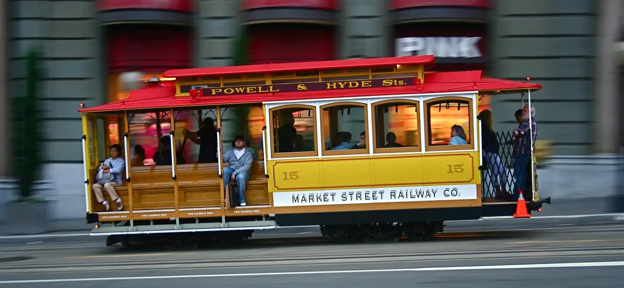 A yellow and red San Francisco cable car moving along Market Street in daylight