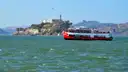 A red and white bay ferry crossing San Francisco Bay with Alcatraz Island behind it