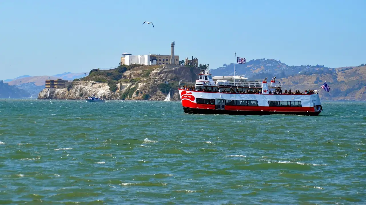 A red and white bay ferry crossing San Francisco Bay with Alcatraz Island behind it