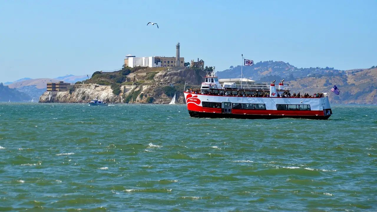 A red and white bay ferry crossing San Francisco Bay with Alcatraz Island behind it