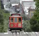 A red cable car coming up a steep San Francisco hill