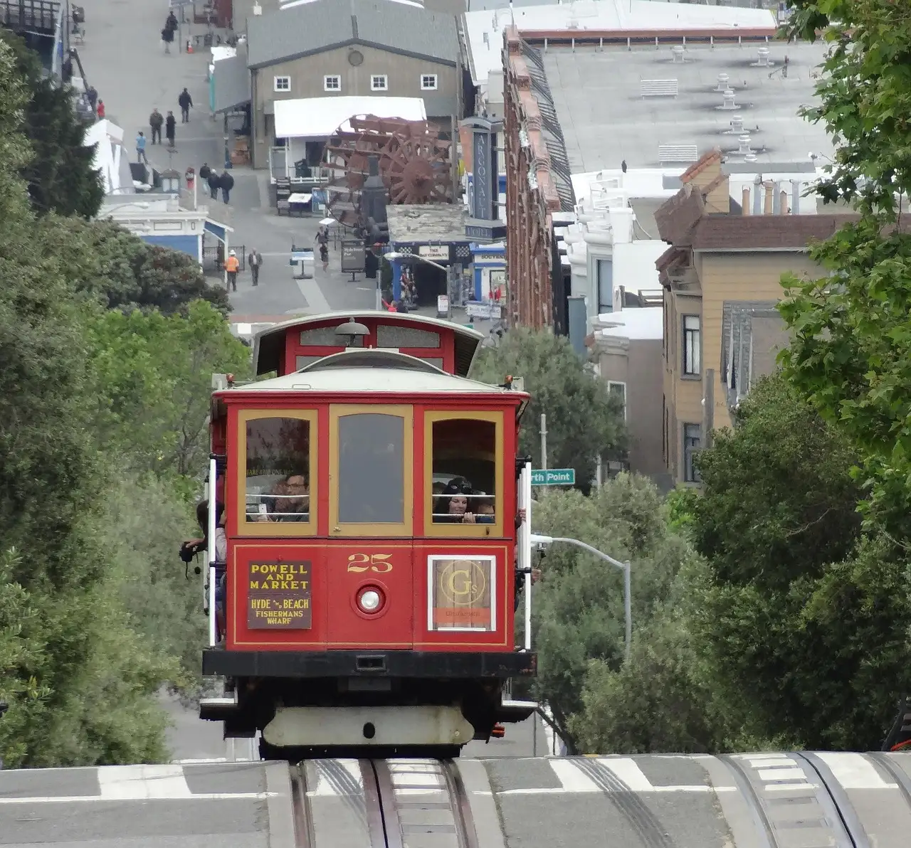A red cable car coming up a steep San Francisco hill