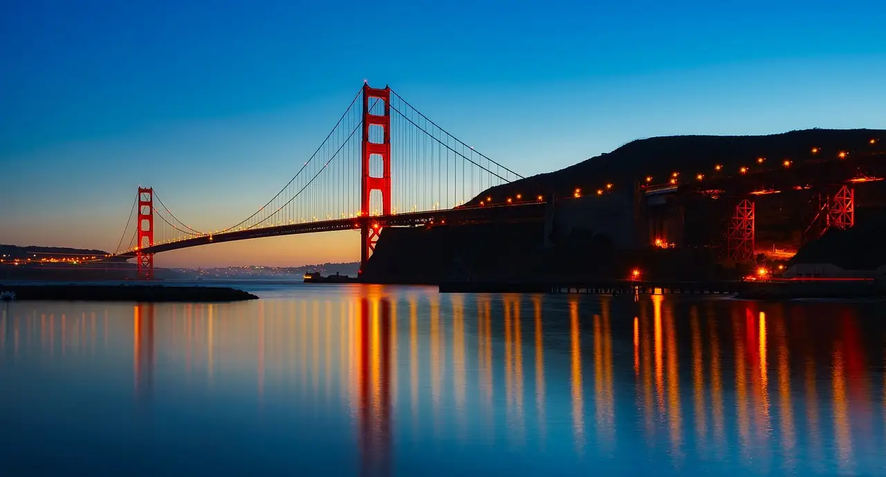 The Golden Gate Bridge and its lights reflected in the bay at dusk