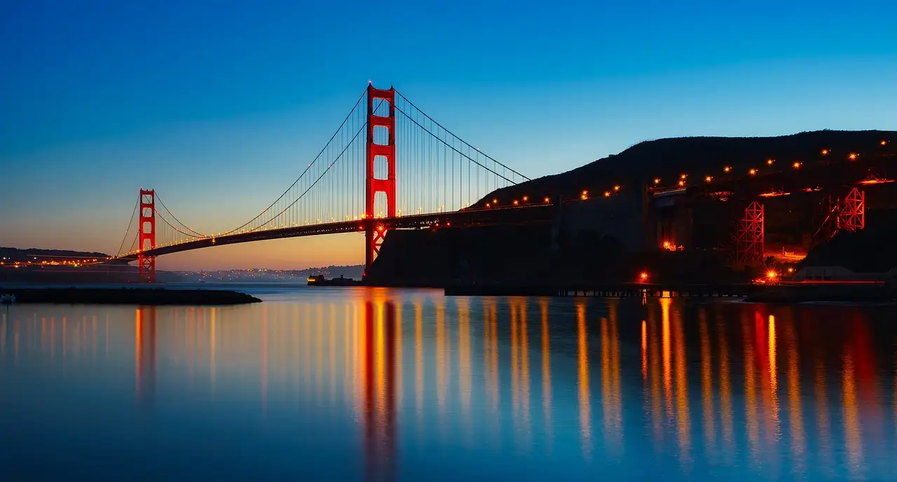 The Golden Gate Bridge and its lights reflected in the bay at dusk