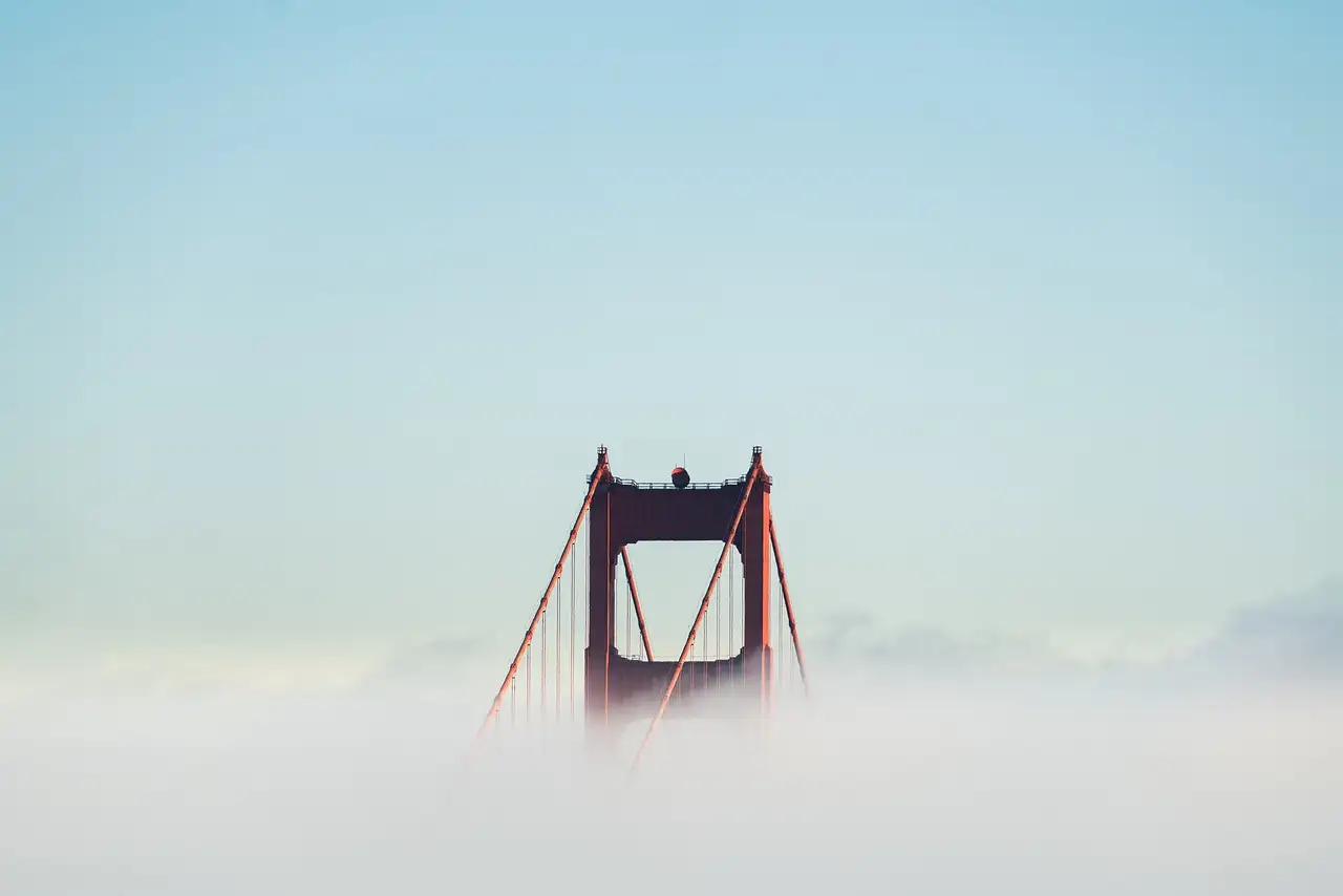 The top of a Golden Gate Bridge tower rising out of a layer of fog