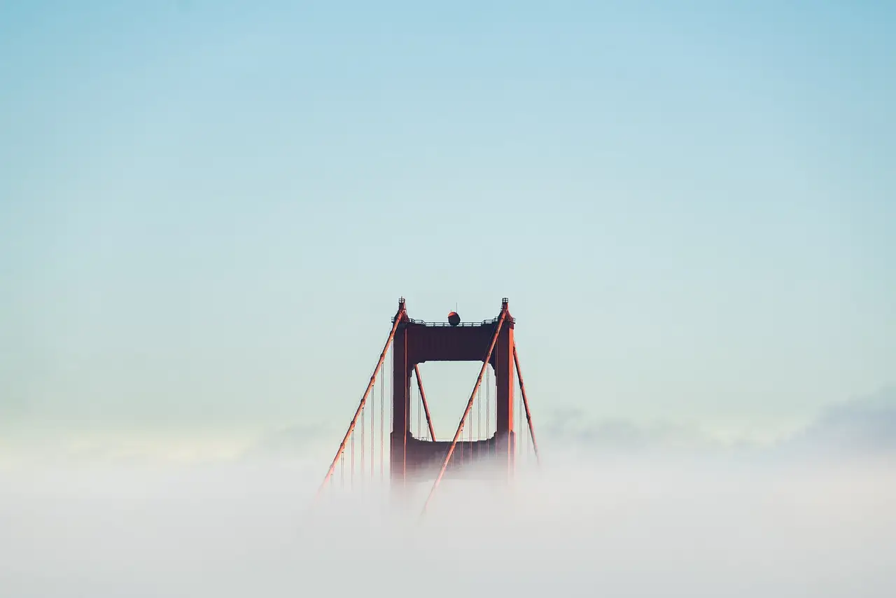 The top of a Golden Gate Bridge tower rising out of a layer of fog