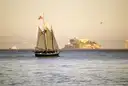 A schooner under sail on San Francisco Bay in evening light, with Alcatraz behind it