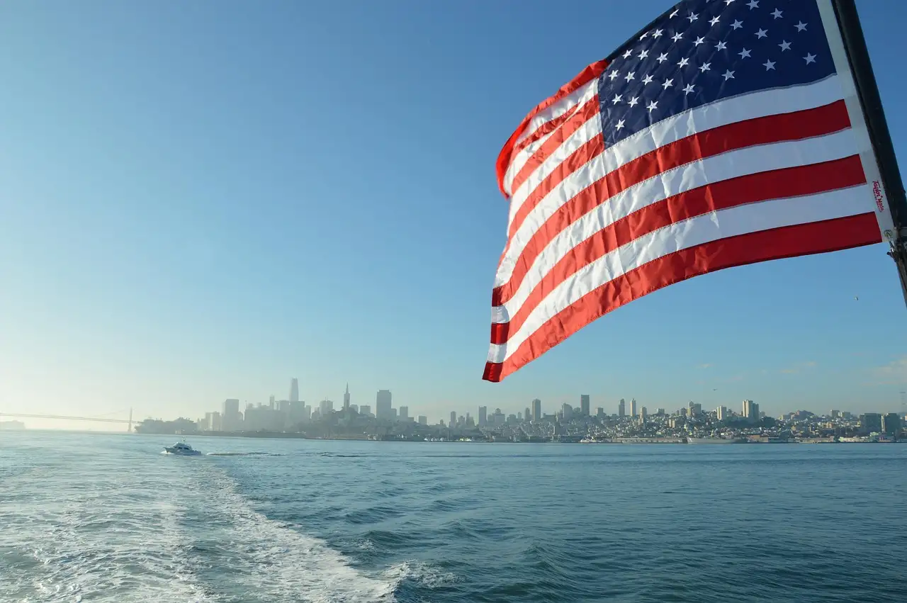 The San Francisco skyline seen from the back of a boat, with a US flag