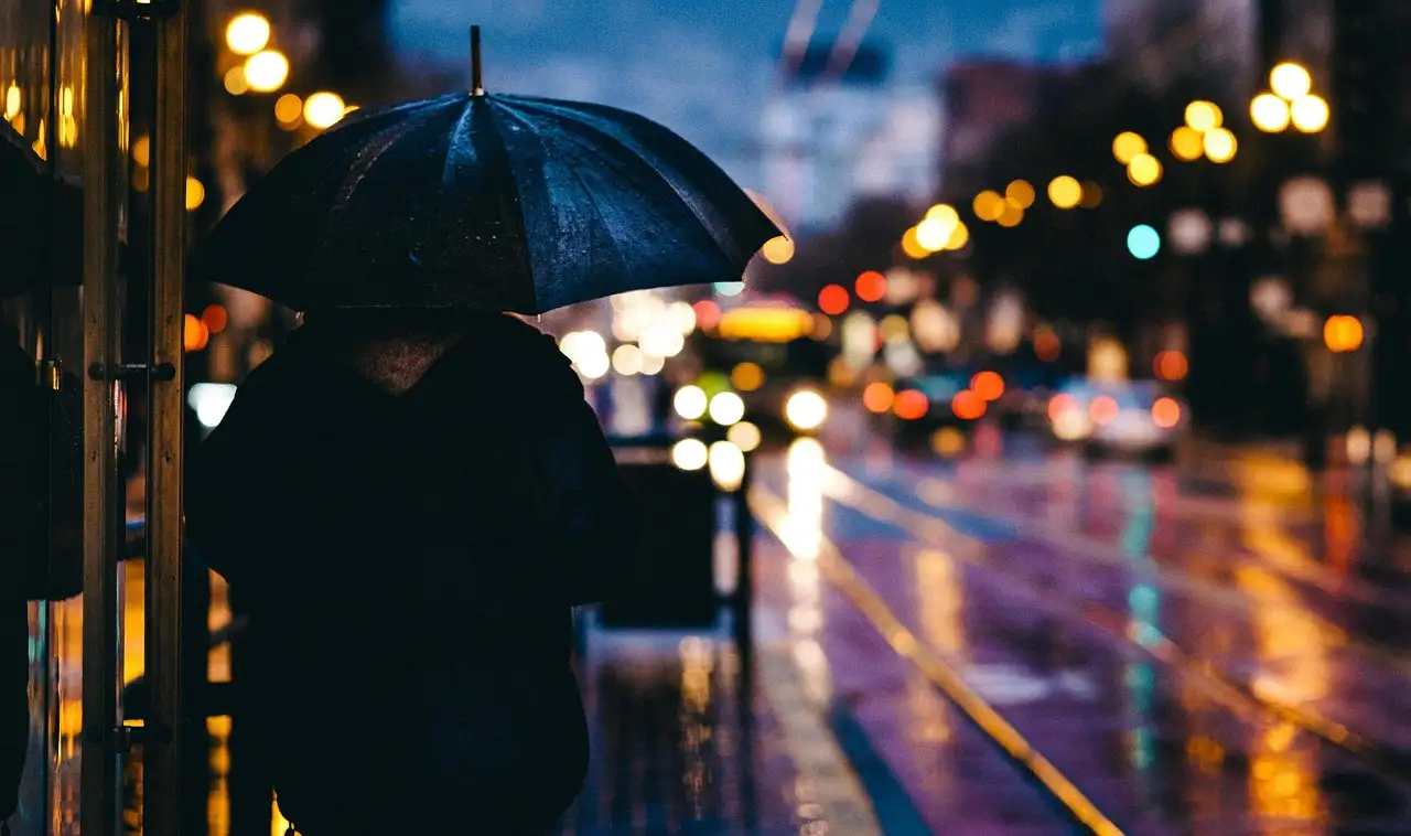 A person under an umbrella on a rainy San Francisco street with cable car tracks and city lights
