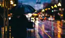 A person under an umbrella on a rainy San Francisco street with cable car tracks and city lights