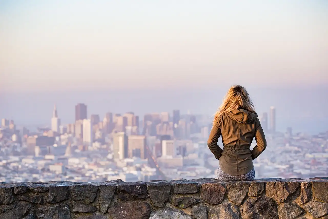 A visitor looking out over the San Francisco skyline from a stone wall on a hilltop