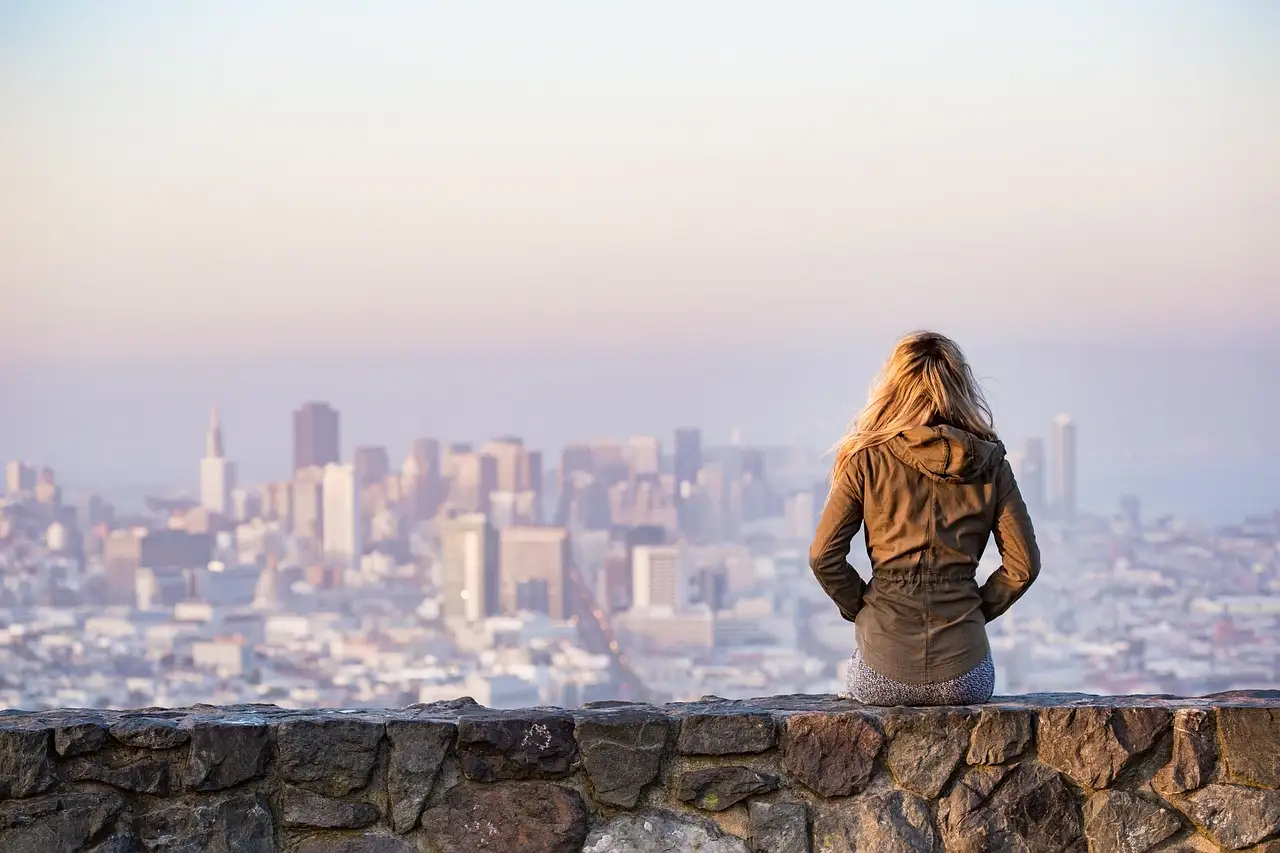 A visitor looking out over the San Francisco skyline from a stone wall on a hilltop