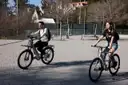 Two riders on e-bikes crossing a sunny plaza