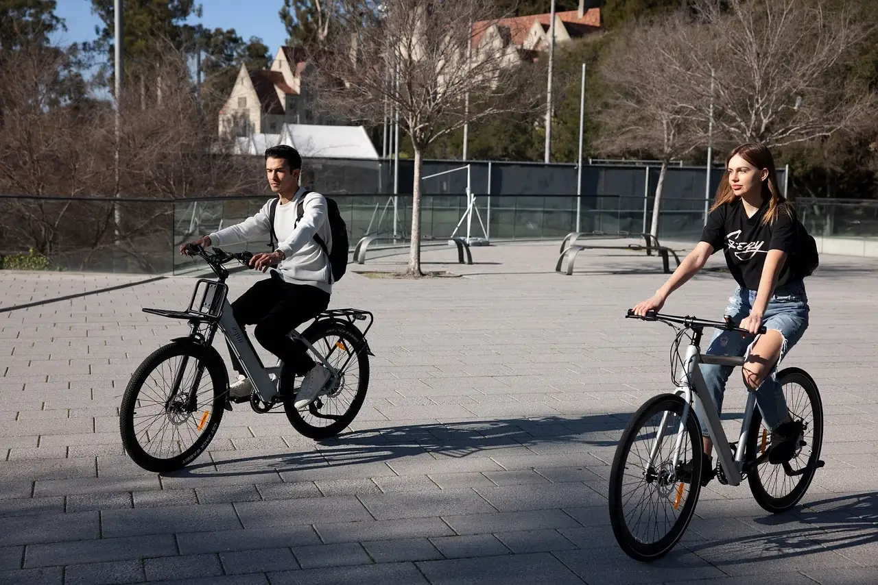 Two riders on e-bikes crossing a sunny plaza