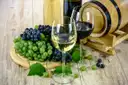 A glass of white and a glass of red wine next to grapes and a small barrel
